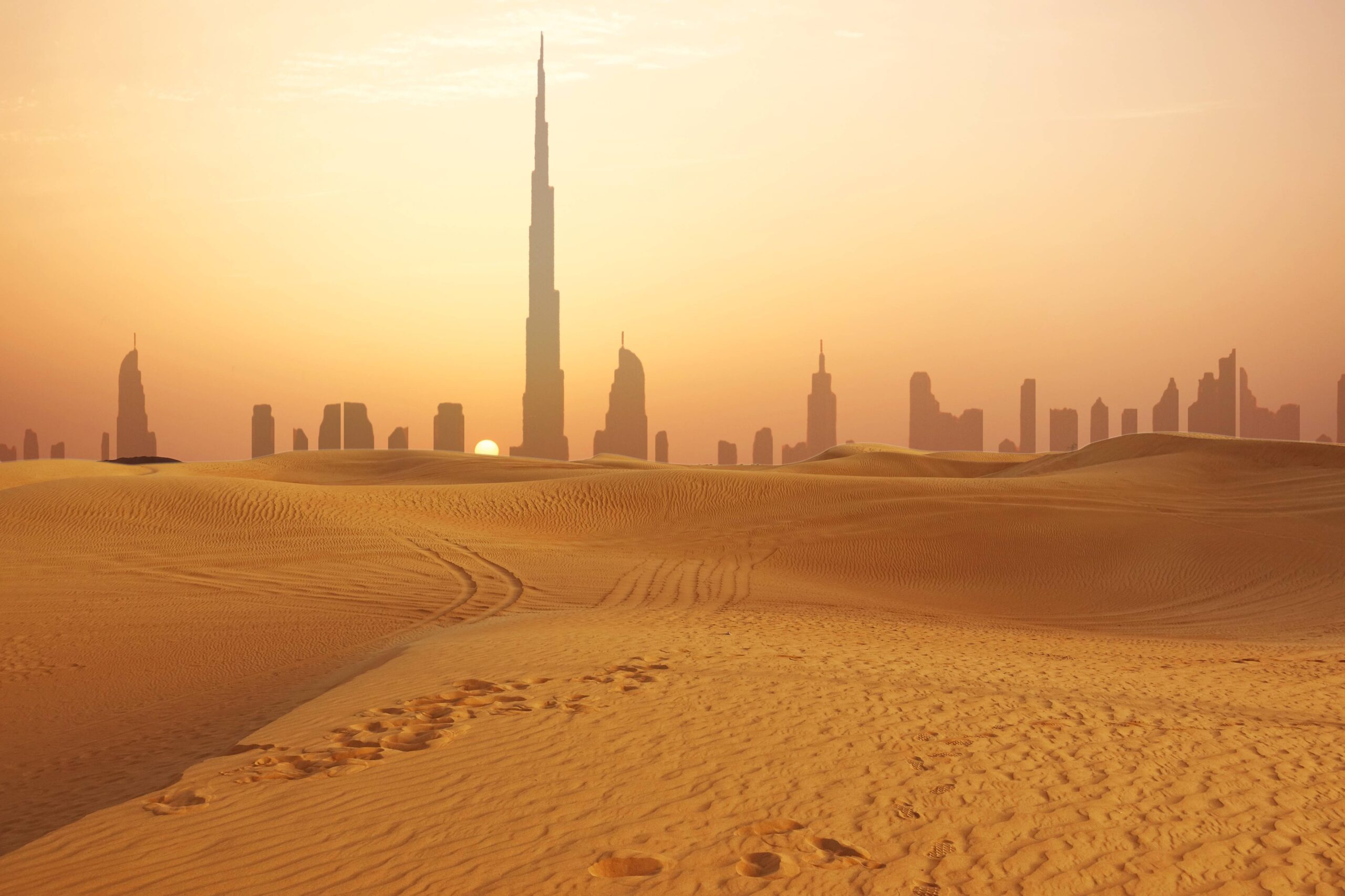 Dunes de sable au coucher du soleil avec la Burj Khalifa en arrière-plan.